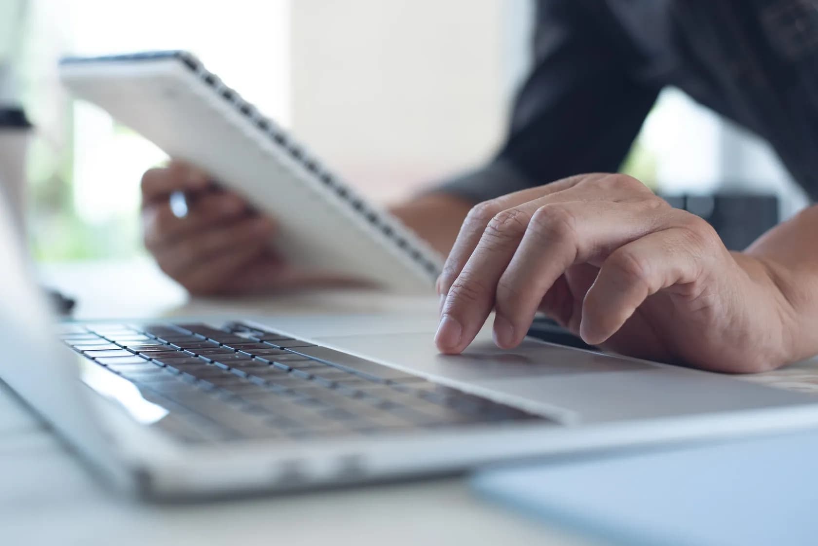 Man typing on a laptop while referencing a notepad